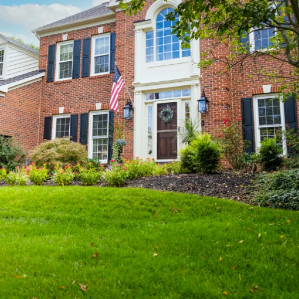 An American brick house sits behind a green lawn